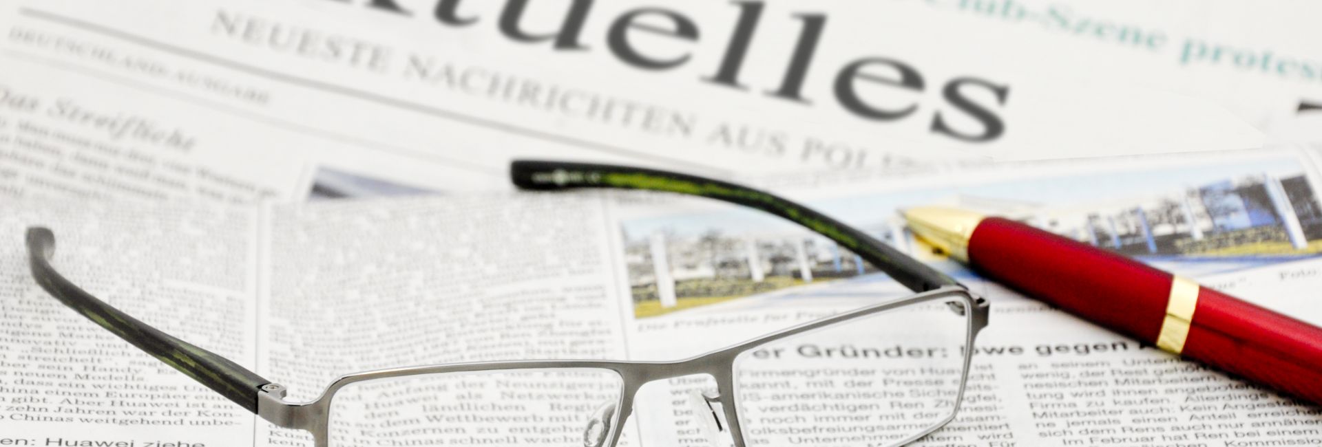 Brille und Stift auf einer Zeitung Rubrik Aktuelles liegend