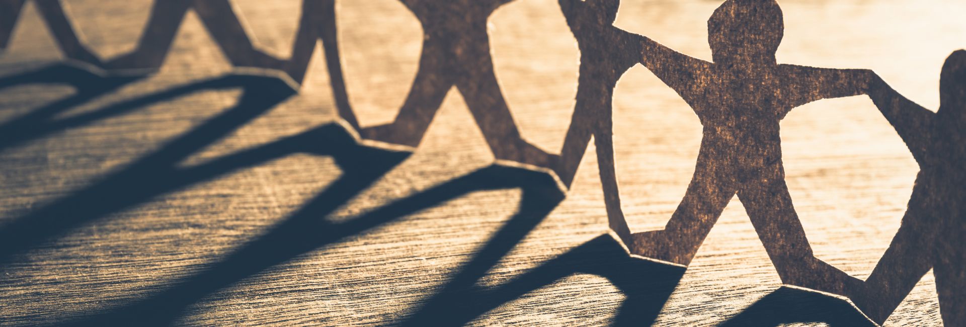 Ausgeschnittene Papier-Männchen, die sich an den Händen halten und einen Kette bildend. Stehen auf einem Tisch und werfen Schatten.